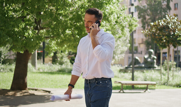 Man in a white shirt taking a phone call outdoors in a park