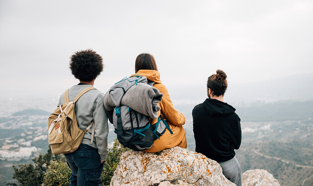 Three friends sitting on a hilltop looking out over a valley