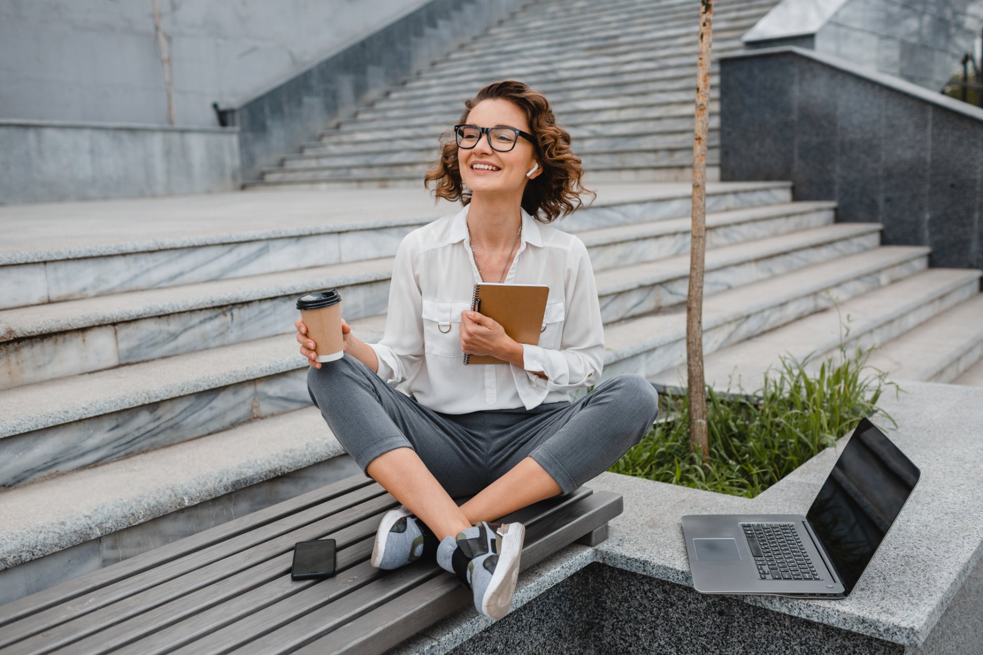 Woman with coffee and notebook sitting on outdoor steps