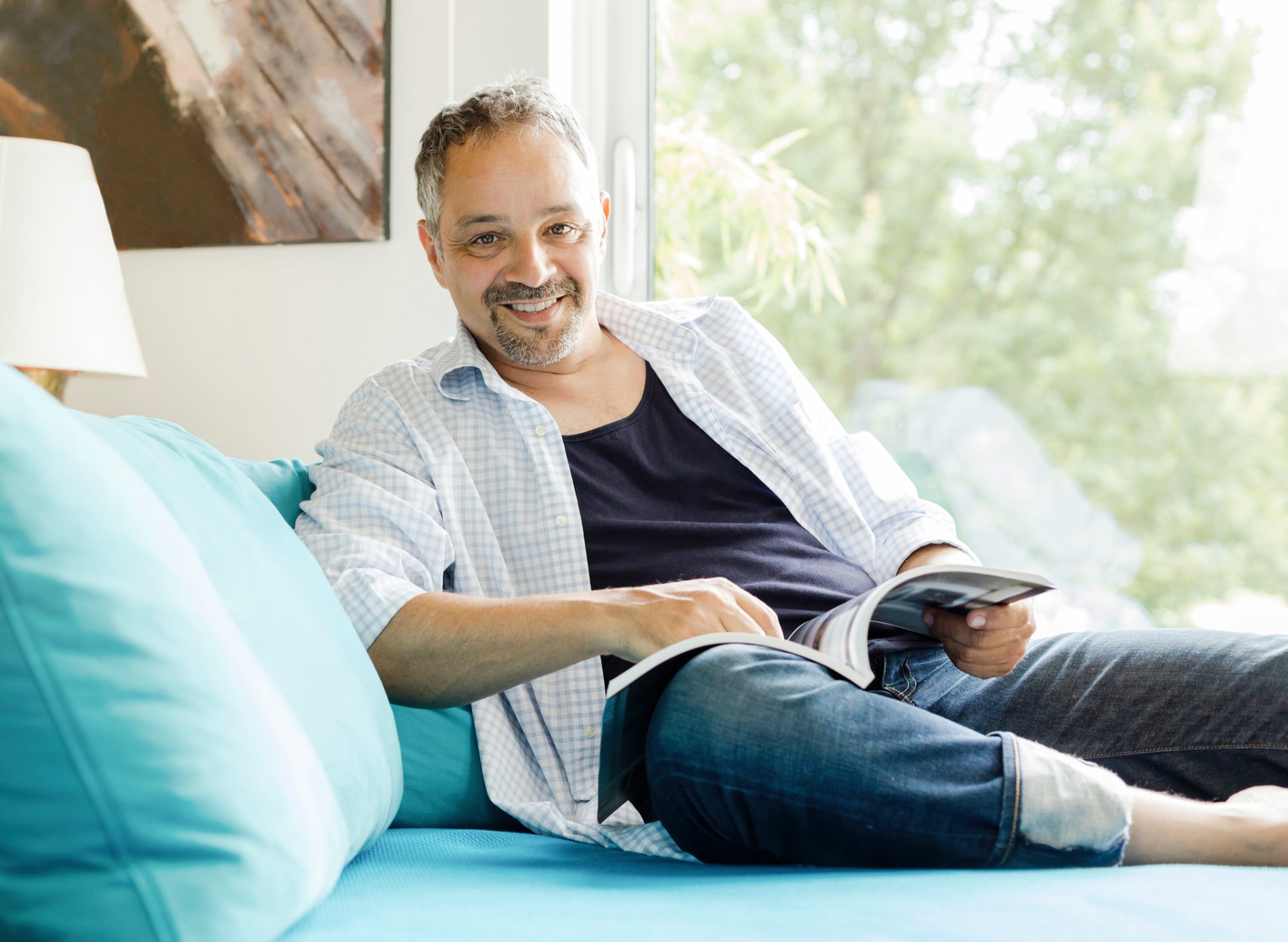 Smiling man reading a magazine on a sofa